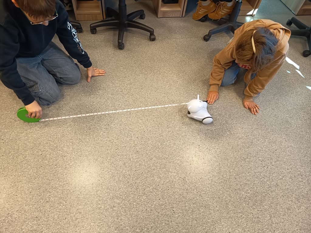 Szóstoklasiści mierzący długość boku prostokąta tworzonego na podłodze przez robota Photon