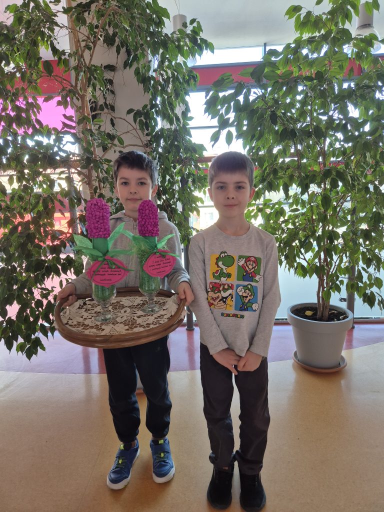 Dominik i Mikołaj z 1a na szkolnym korytarzu trzymają tacę z hiacyntami. 