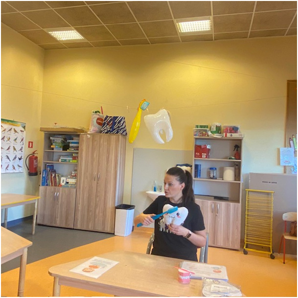 Pani asystentka stomatologiczna pokazuje techniki prawidłowego szczotkowania na pluszowym ząbku.