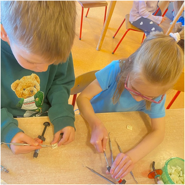 Uczeń i uczennica przy pomocy narzędzi stomatologicznych (nakładacz i kulka) wypełniają modelowy ząb materiałem kompozytowym.