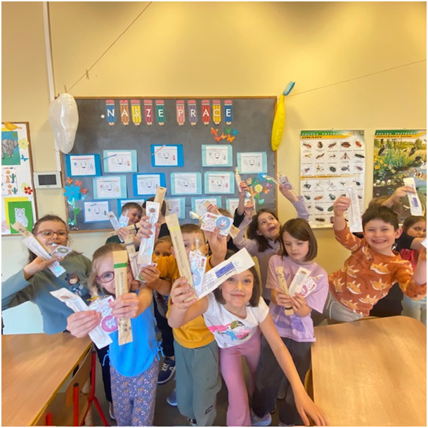 Uczniowie z grupy III świetlicowej z wręczonym zestawem upominkowym (szczoteczki, lusterka stomatologiczne, harmonogram mycia zębów) oraz uśmiechem na twarzach.